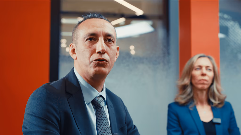 Intervenant en costume prenant la parole lors du webinaire Carac tourné en faux direct, une intervenante en arrière-plan