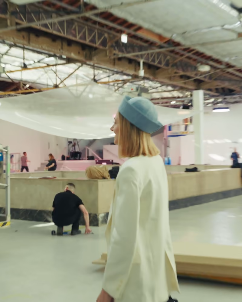 Une jeune femme au chapeau bleu traverse le hall où se prépare le défilé Istituto Marangoni