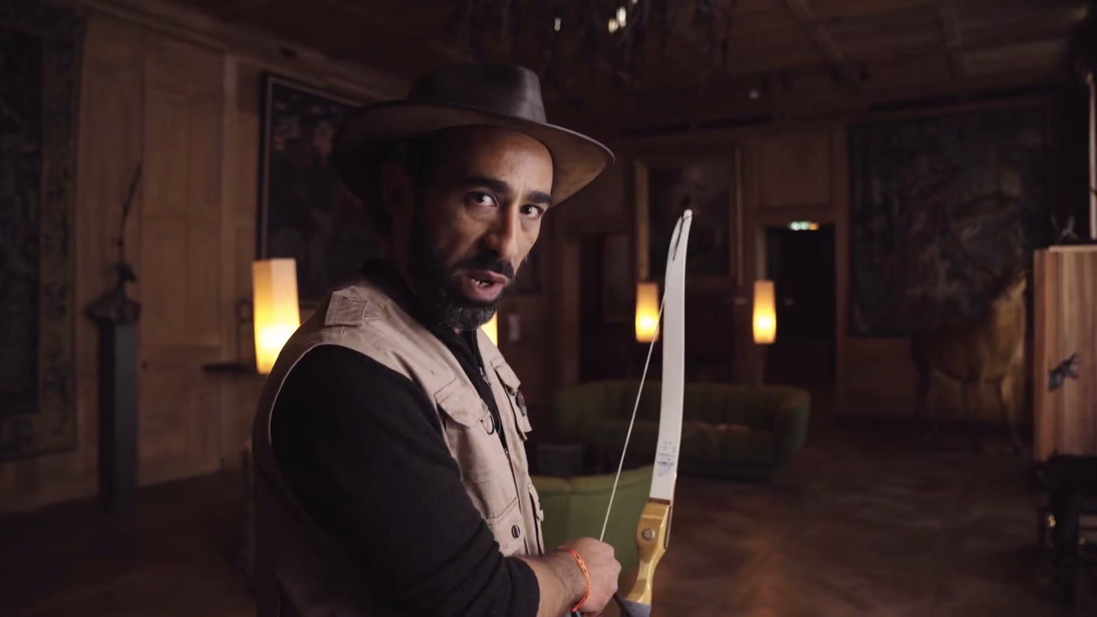 Un comédien coiffé d’un chapeau, un arc à la main, dans un salon du musée