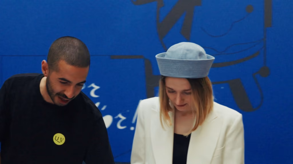 Deux étudiants en coulisses du défilé Istituto Marangoni, devant un mur bleu illustré