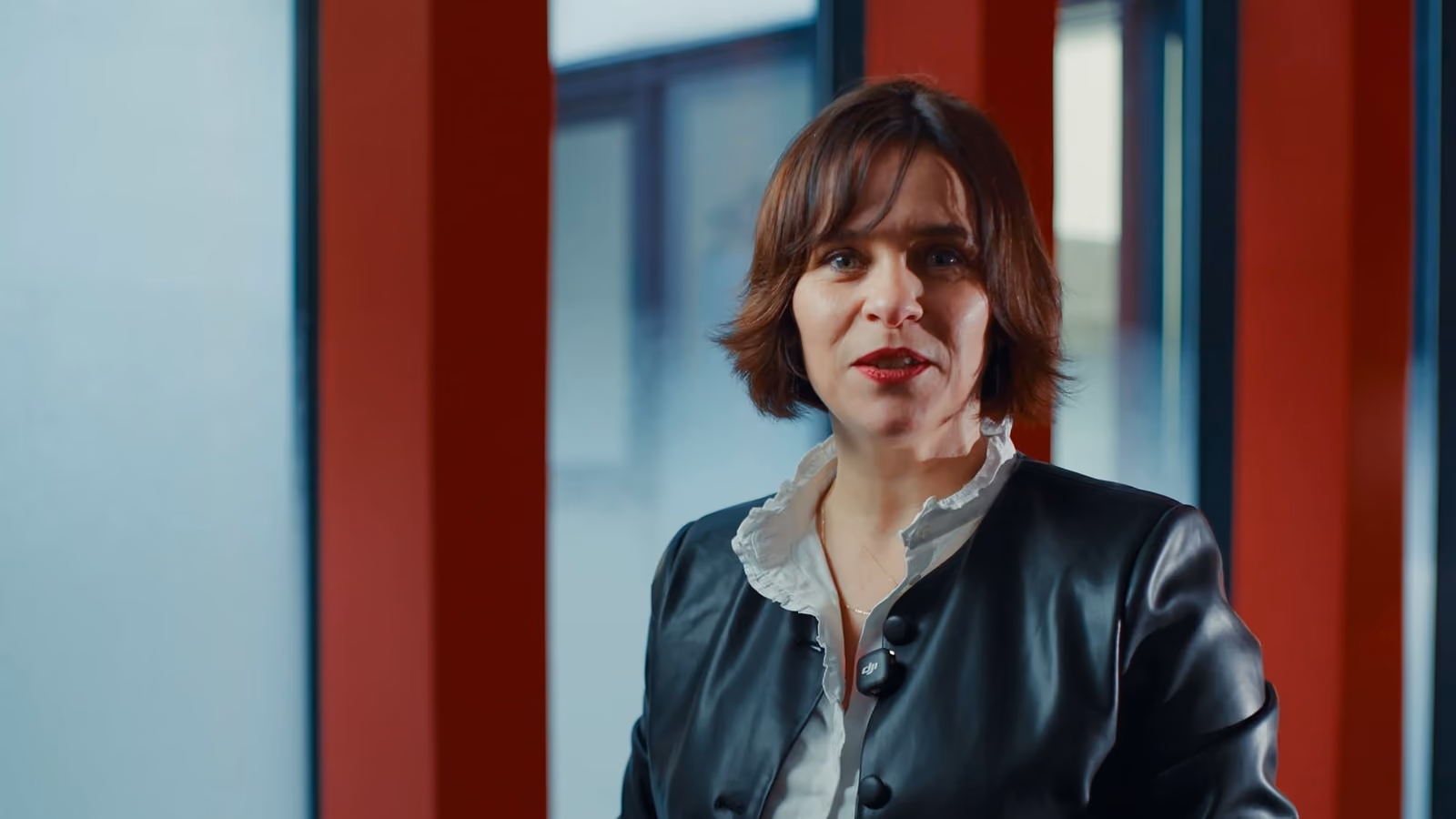 Intervenante face caméra devant les fenêtres et les murs rouges des locaux Carac, teaser multicaméra
