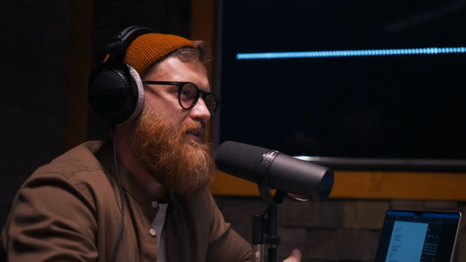 Un homme parle au micro dans un studio de podcast, casque sur les oreilles.